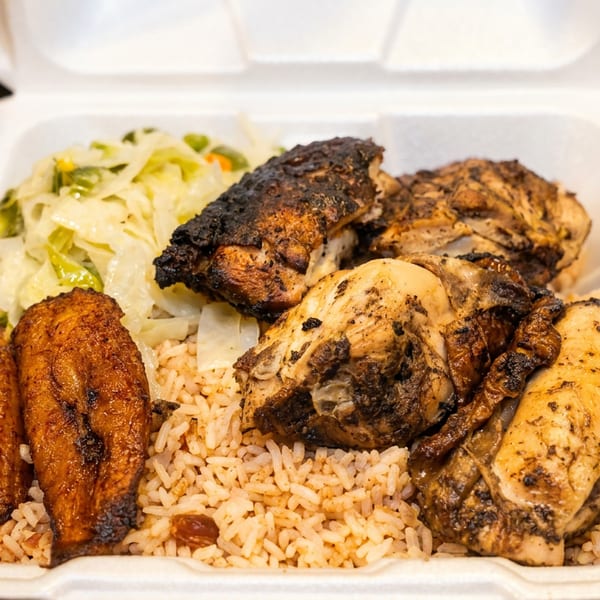 Jerk chicken, rice and peas, cabbage, and plantains in a white takeout container.
