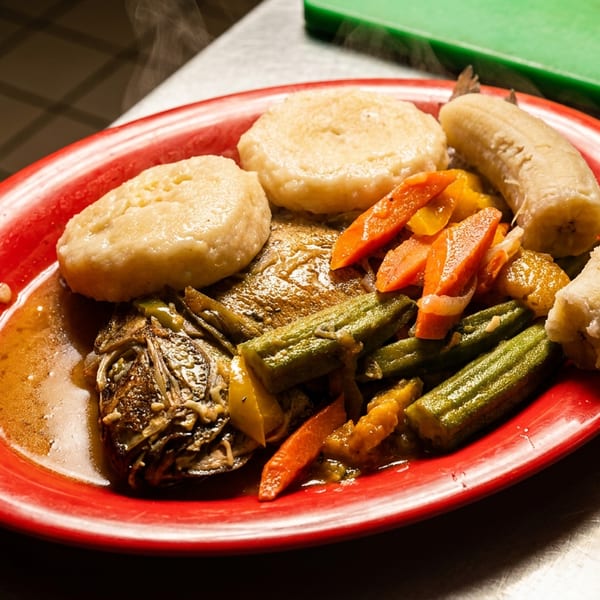 Steaming whole fish with dumplings, okra, carrots, and bananas on a red plate.